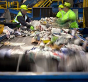 Workers separating paper and plastic on a conveyor belt in a recycling facility